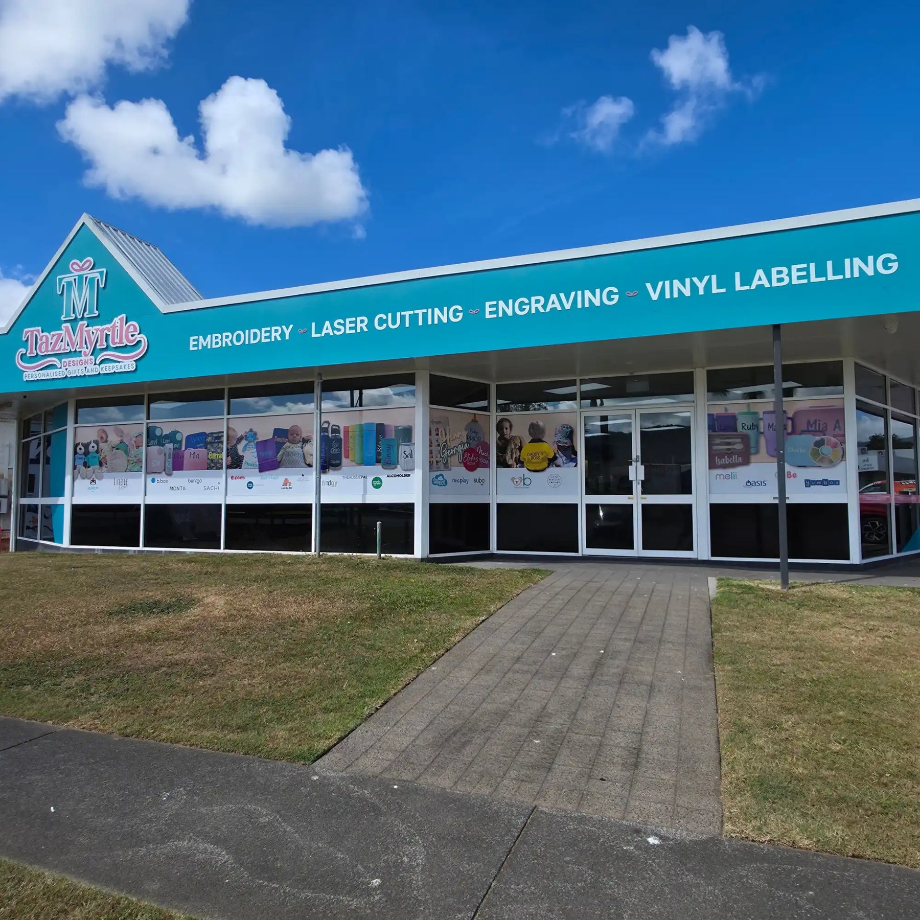 Teal storefront with white trim and green roof, displaying various products through large windows.
